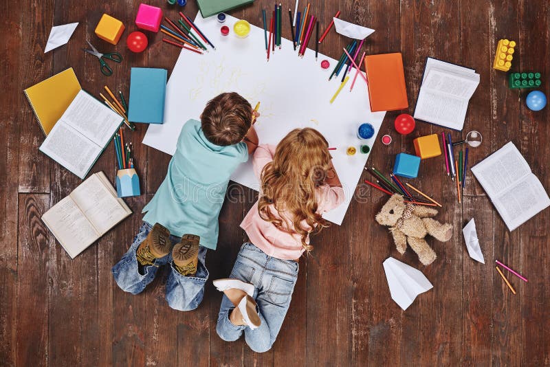 Play is the work of childhood. Children lying near books and toys, while drawing stock photos Play is the work of childhood. Children lying near books and toys, while drawing stock photos