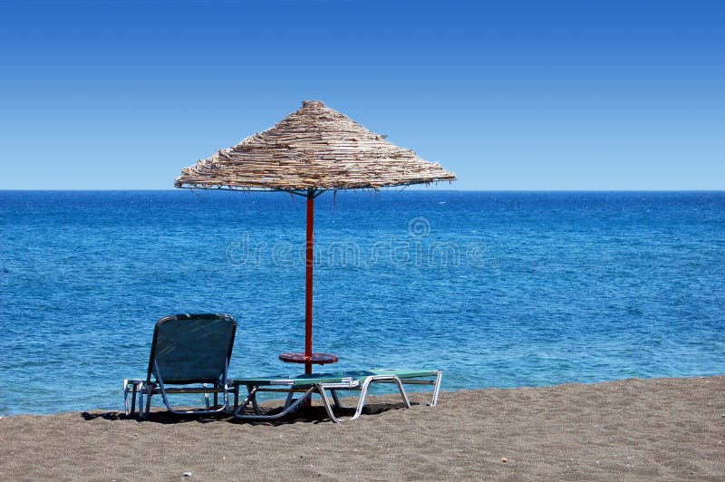 An umbrella and sun bathing chairs on the black beach of Perissa, in the Greek Islands. An umbrella and sun bathing chairs on the black beach of Perissa, in the Greek Islands.