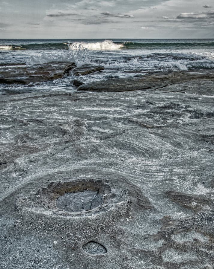 Playa rocosa con el cráter de luna como superficie, ondas y nubes fotografía de archivo Playa rocosa con el cráter de luna como superficie, ondas y nubes fotografía de archivo