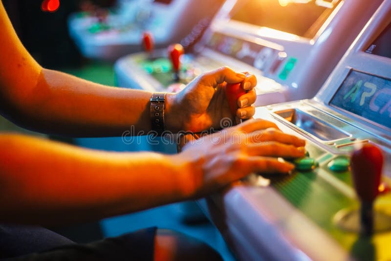 Player`s hands holding a joystick and buttons while playing on a white arcade video game