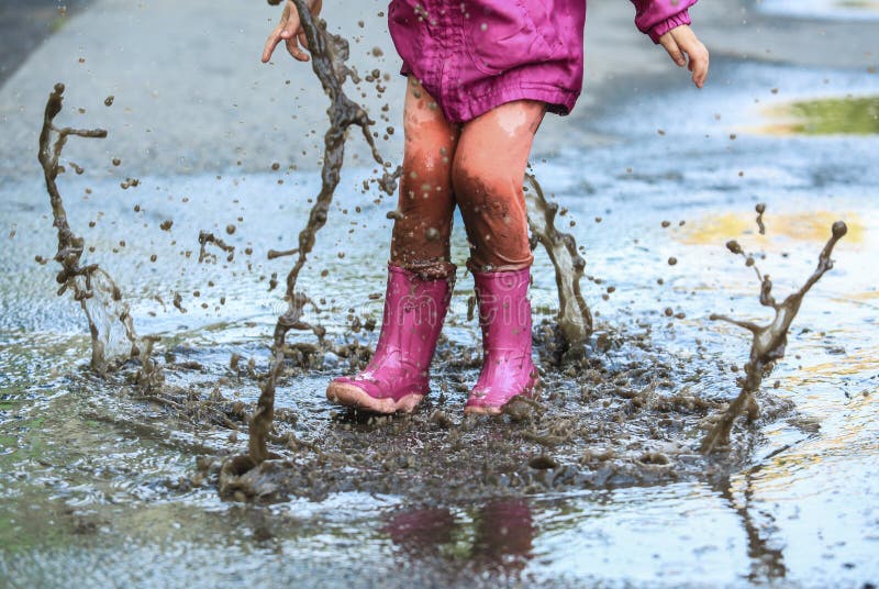 Child outdoor jump into puddle in boot after rain