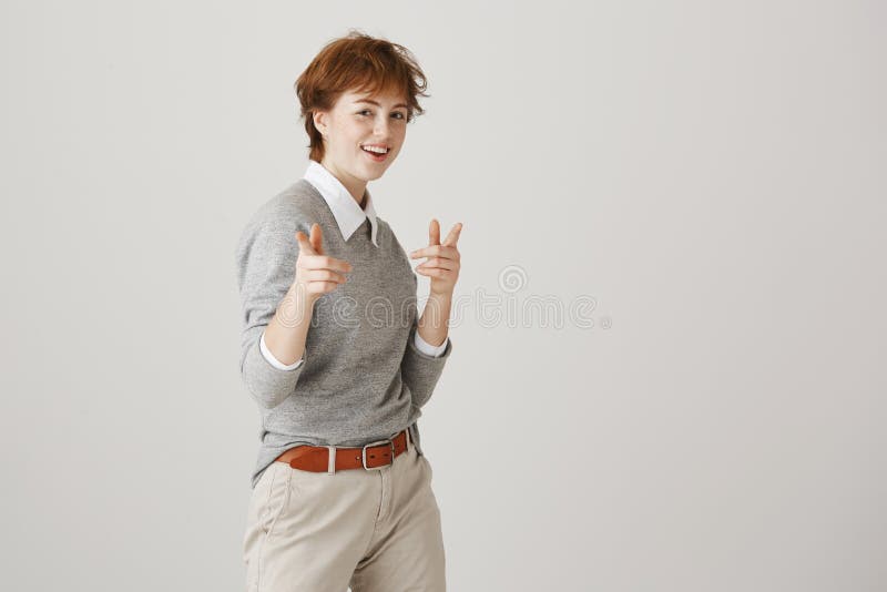 Playful emotive redhead female with boyish messy hairstyle and outfit showing guns gesture or pointing at camera