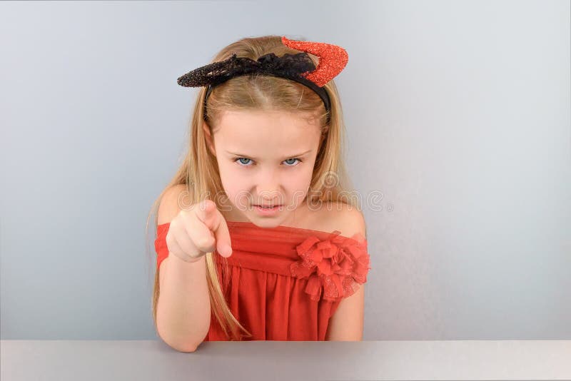 Playful little girl in red demon costume portrays an evil face and pointing finger at you