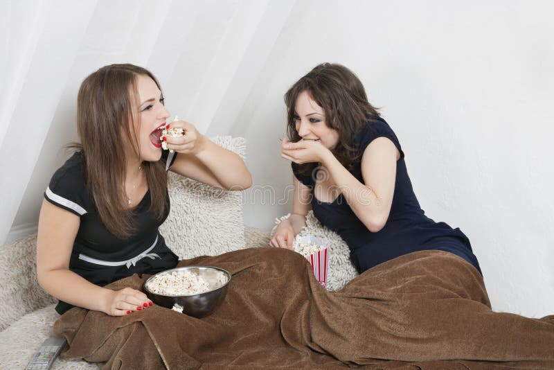 Playful young women eating popcorn in bed