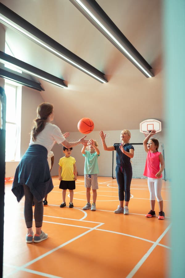 Sports Teacher Throwing Ball To Her Pupils. Stock Photo