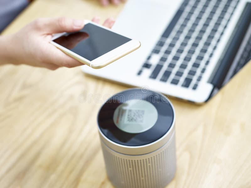 Hand of a person holding cellphone playing music through a portable blue-tooth speaker.