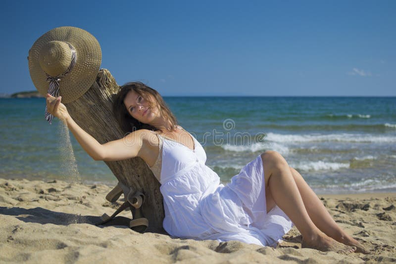 Krásná mladá žena leží na písečné pláži na sobě klobouk a bílé šaty, užívat si slunce.