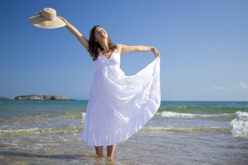 Bella giovane donna che indossa un cappello e un vestito bianco a giocare con le onde del mare.
