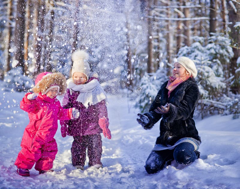 Matka a dvě děti si hrají se sněhem v zimě lese.