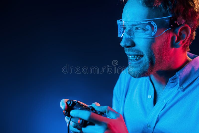 Plays game by using controller. Neon lighting. Young european man is in the dark studio
