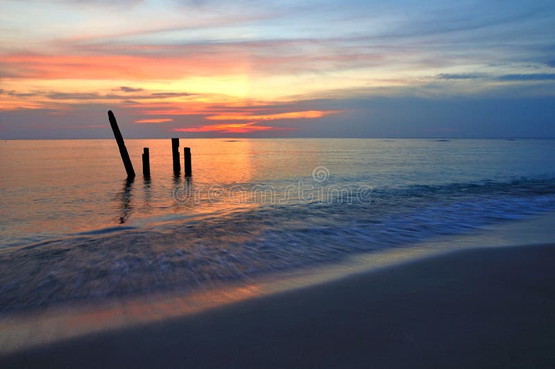 Picturesque sunset over wooden posts in calm sea with beach in foreground. Picturesque sunset over wooden posts in calm sea with beach in foreground.