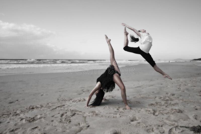 Two athletic girls vigorously dancing and leaping on a sandy beach. Color desaturated. Two athletic girls vigorously dancing and leaping on a sandy beach. Color desaturated