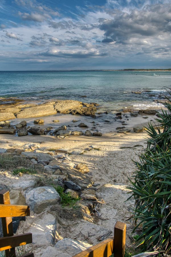 Plażowi wejściowi stopa druki w piasek miękkiej części machają niebieskie niebo z chmurami, surfingowowie w odległości obrazy royalty free Plażowi wejściowi stopa druki w piasek miękkiej części machają niebieskie niebo z chmurami, surfingowowie w odległości obrazy royalty free