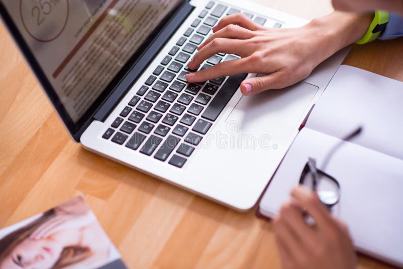 Modern helper. Close up of pleasant person sitting at the table and working on the laptop while typing.