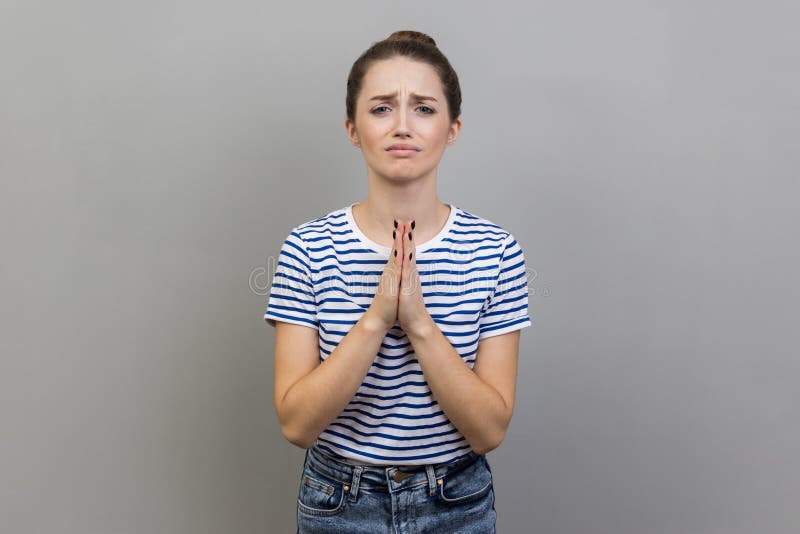 Woman holding hands in prayer and asking for help with pleading imploring expression, full of hope.