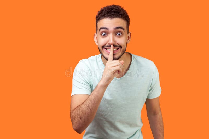 Please, keep silence! Portrait of positive brunette man asking to be quiet. indoor studio shot isolated on orange background