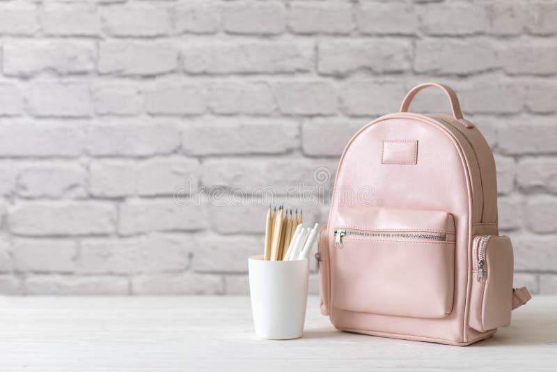 Female school backpack with stationery supplies on desk at white loft brick background. Elegant bag for carrying schooler accessories with notebook, pencil and sketchbook. Back to school concept. Female school backpack with stationery supplies on desk at white loft brick background. Elegant bag for carrying schooler accessories with notebook, pencil and sketchbook. Back to school concept