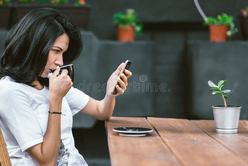 Plenerowy strzał Kaukaska dziewczyna w białej koszulce cieszy się bezpłatnego fi przy sklepem z kawą, surfujący internet na telef zdjęcie royalty free Plenerowy strzał Kaukaska dziewczyna w białej koszulce cieszy się bezpłatnego fi przy sklepem z kawą, surfujący internet na telef zdjęcie royalty free