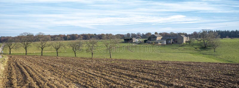 plowed field with meadow and old farm in belgian ardennes near namur under blue sky in the fall