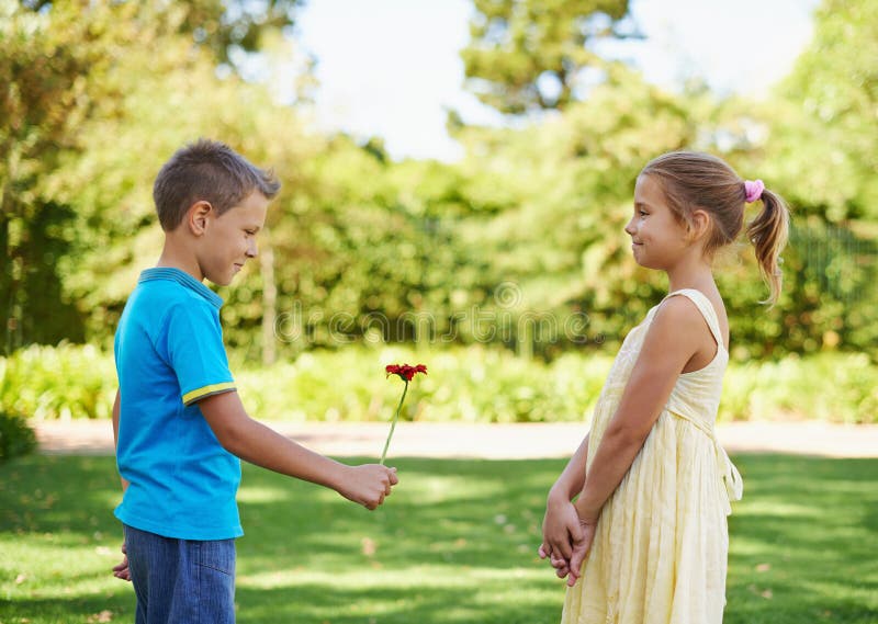 Plucking up the courage. A bashful little boy holding a flower out to the little girl he has a crush on.