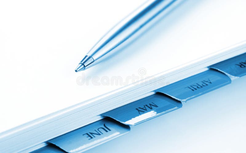 Silver ballpoint pen on a day planner file. Soft focus on pen point. Blue tone. Silver ballpoint pen on a day planner file. Soft focus on pen point. Blue tone.