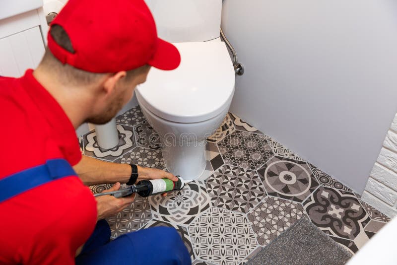 Plumber applying silicone sealant around water closet stock photo Plumber applying silicone sealant around water closet stock photo