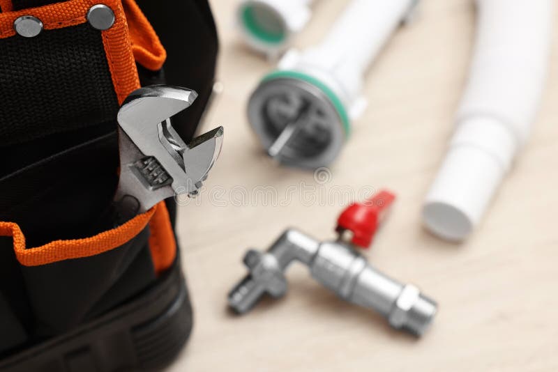 Plumber`s tool bag with adjustable wrench and pipes on table, closeup. Space for text