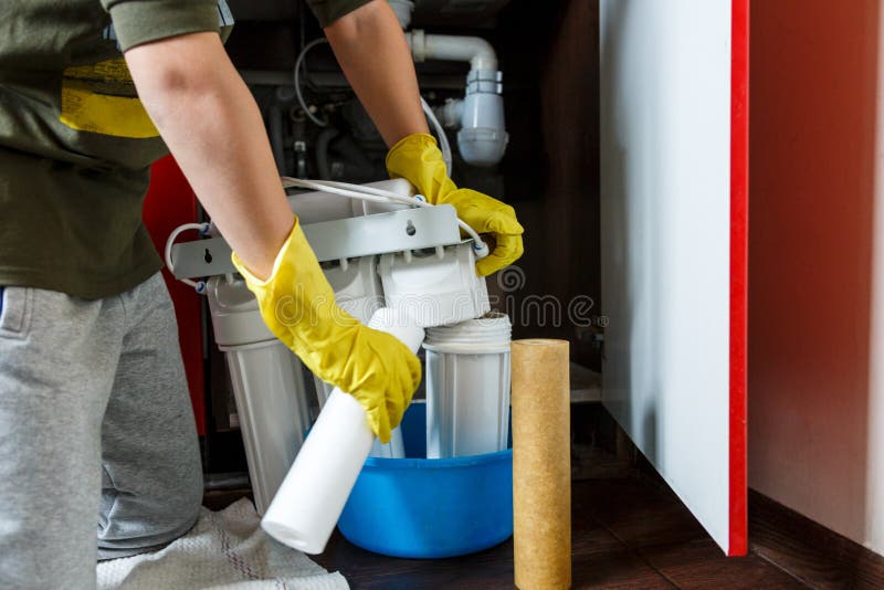 Plumber in yellow household gloves changes water filters. Repairman installing water filter cartridges in kitchen. royalty free stock images Plumber in yellow household gloves changes water filters. Repairman installing water filter cartridges in kitchen. royalty free stock images