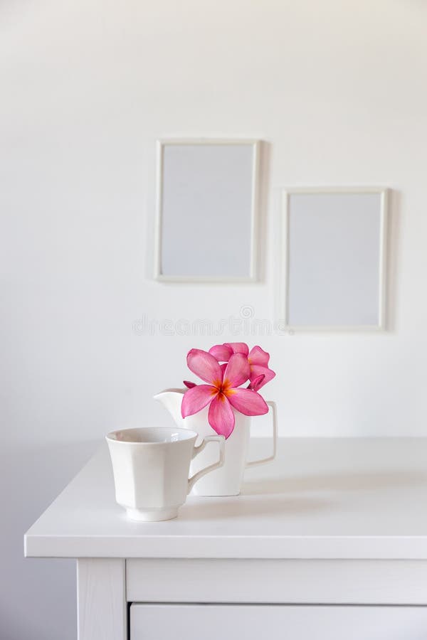 Plumberia rumba in a mug, and cup of coffee on a white table against a wall with two frames. Ready layout. Vertical frame. Space for text. Plumberia rumba in a mug, and cup of coffee on a white table against a wall with two frames. Ready layout. Vertical frame. Space for text