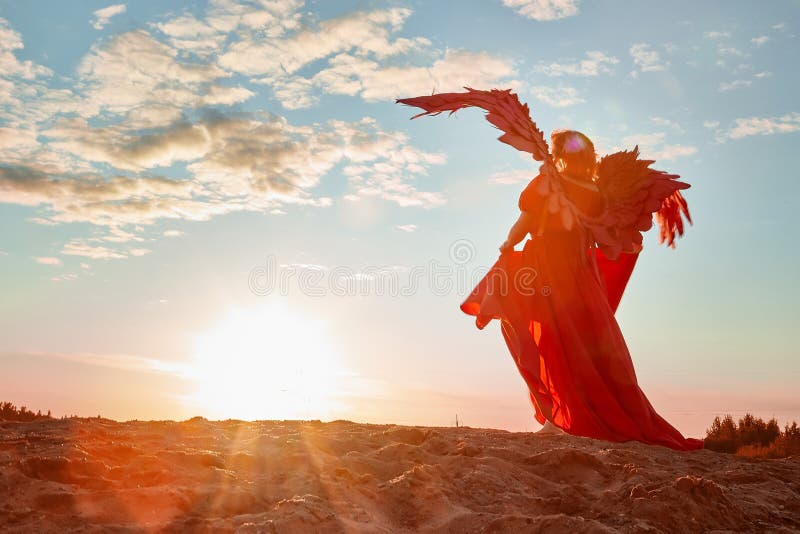 A plump blonde middle-aged woman with red angle wings in a desert with dunes and sand in a nice summer or spring sunny