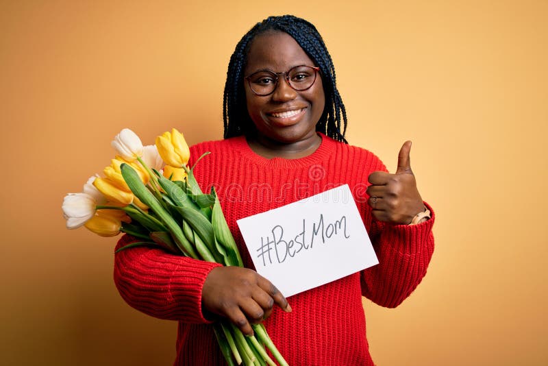 Plus size african american woman holding best mom message and tulips on mothers day happy with big smile doing ok sign, thumb up with fingers, excellent sign. Plus size african american woman holding best mom message and tulips on mothers day happy with big smile doing ok sign, thumb up with fingers, excellent sign