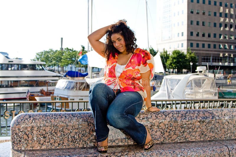 Beautiful plus size woman sitting at a marina catching a breeze and holding hair. Beautiful plus size woman sitting at a marina catching a breeze and holding hair