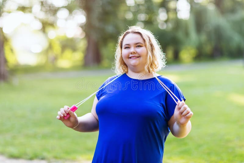 Plus size blonde girl with a skipping rope in her hands posing in a park. Healthy lifestyle concept.