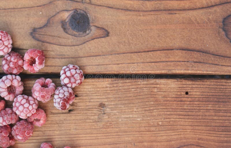 Plusieurs framboises surgelées, couvertes de fruit, se trouvent sur le fond en bois image stock Plusieurs framboises surgelées, couvertes de fruit, se trouvent sur le fond en bois image stock