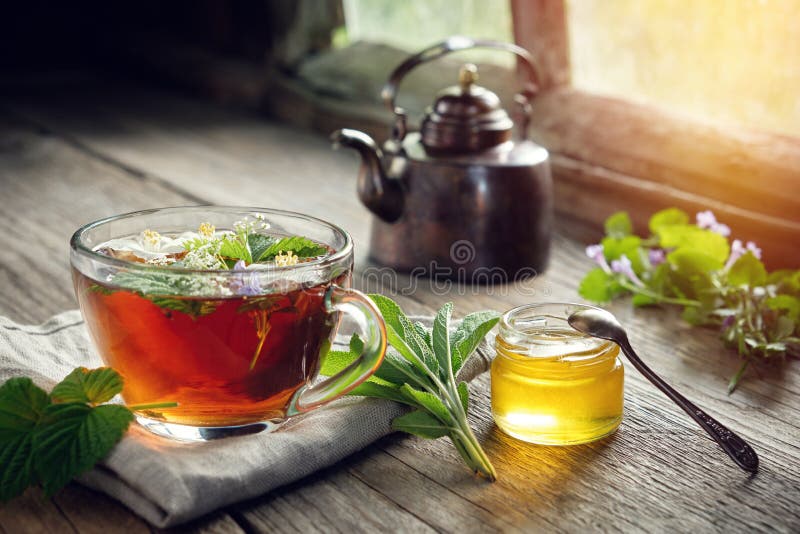 Plusieurs plantes médicinales et herbes sur la table, la tasse de tisane saine, le pot de miel et la bouilloire de thé d'en cuivr