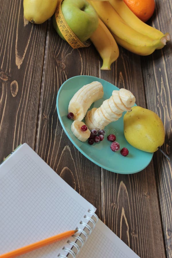 Plátanos, corte en un plato con el arándano congelado y cuaderno fotografía de archivo Plátanos, corte en un plato con el arándano congelado y cuaderno fotografía de archivo