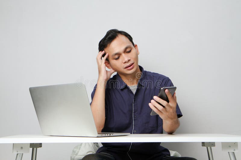 Plötslig, förvirrad som man som håller mobiltelefon medan man sitter framför den bärbara datorn. isolerad bakgrund royaltyfria foton