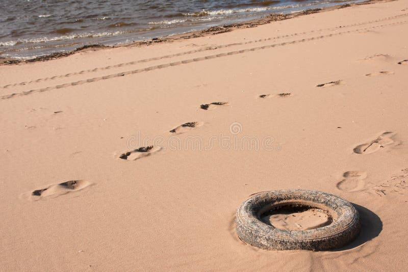 Pneu de carro poluir na areia na praia perto da água imagem de stock Pneu de carro poluir na areia na praia perto da água imagem de stock