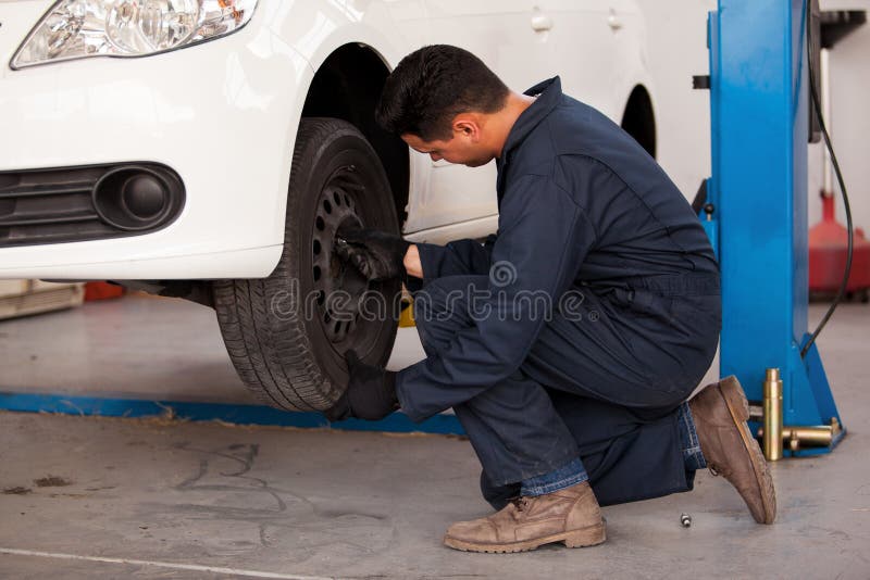 Young mechanic rotating tires of a suspended car at an auto shop. Young mechanic rotating tires of a suspended car at an auto shop