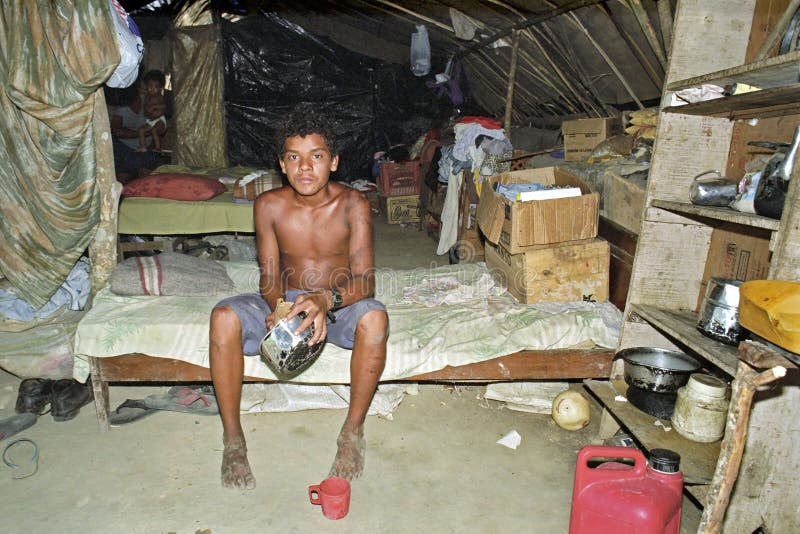 Brazil, state of Espirito Santo in the place Cachoeiro de Itapemirim have the landless and homeless people builded a camp, the residents called it Nova Safra. The poor housing is made of plastic and wood. In one such hut a young man is eating out of a cooking pot, sitting on his bed. His meager belongings are in boxes lying around his bed. In a simple wood cabinet are kitchen utensils, cookware. Brazil, state of Espirito Santo in the place Cachoeiro de Itapemirim have the landless and homeless people builded a camp, the residents called it Nova Safra. The poor housing is made of plastic and wood. In one such hut a young man is eating out of a cooking pot, sitting on his bed. His meager belongings are in boxes lying around his bed. In a simple wood cabinet are kitchen utensils, cookware.