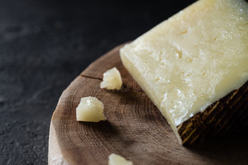 Pocenie ciężkiego sera Hiszpański manchego na drewnianym cięciu na ciemnym nieociosanym tle fotografia royalty free Pocenie ciężkiego sera Hiszpański manchego na drewnianym cięciu na ciemnym nieociosanym tle fotografia royalty free