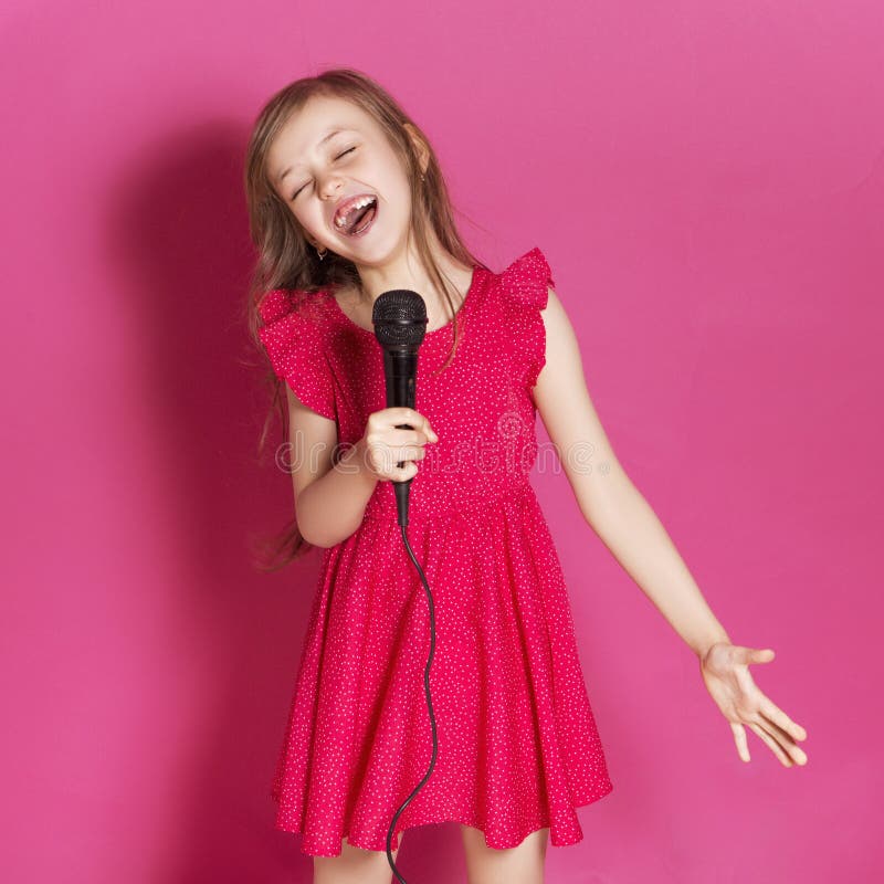 Poco 8 años de la muchacha hace un cierto gesto emocional con su Han. Poco 8 años de la muchacha hace un cierto gesto emocional con sus manos en un fondo neutral rosado Ella tiene vestido rojo moreno largo del verano del pelo y del desgaste Expresión divertida en su cara