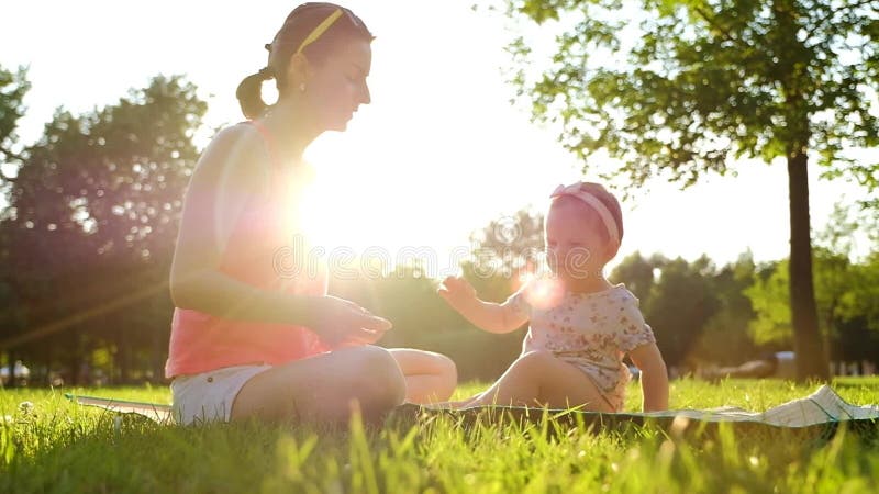 Poco bebé que se sienta con su madre en hierba verde en verano metrajes