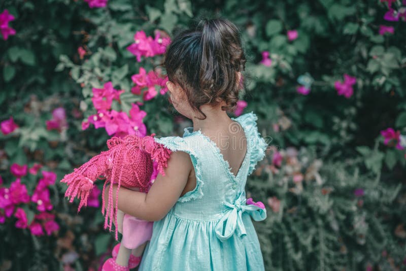 Poco muchacha morena en un vestido del color de la menta en el jardín Muñeca linda de la tenencia del niño foto de archivo Poco muchacha morena en un vestido del color de la menta en el jardín Muñeca linda de la tenencia del niño foto de archivo