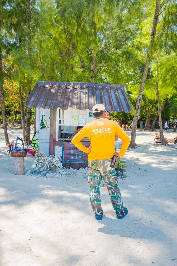 PODA, THAILAND - FEBRUARY 09, 2018: Outdoor view of unidentified man wearing a yellow t-shirt with rescue sign close to a hut of payment fee to enter the phi phi national park on Poda island. PODA, THAILAND - FEBRUARY 09, 2018: Outdoor view of unidentified man wearing a yellow t-shirt with rescue sign close to a hut of payment fee to enter the phi phi national park on Poda island.