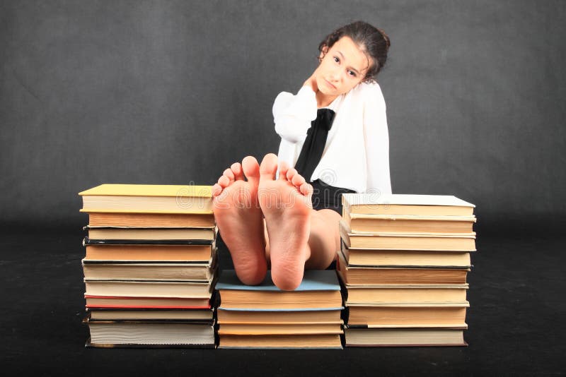 Barefoot schoolgirl dressed in white blouse - soles of bare feet of teenage girl having rest on top stacks of old books on black background. Education and entertainment concept. Barefoot schoolgirl dressed in white blouse - soles of bare feet of teenage girl having rest on top stacks of old books on black background. Education and entertainment concept.