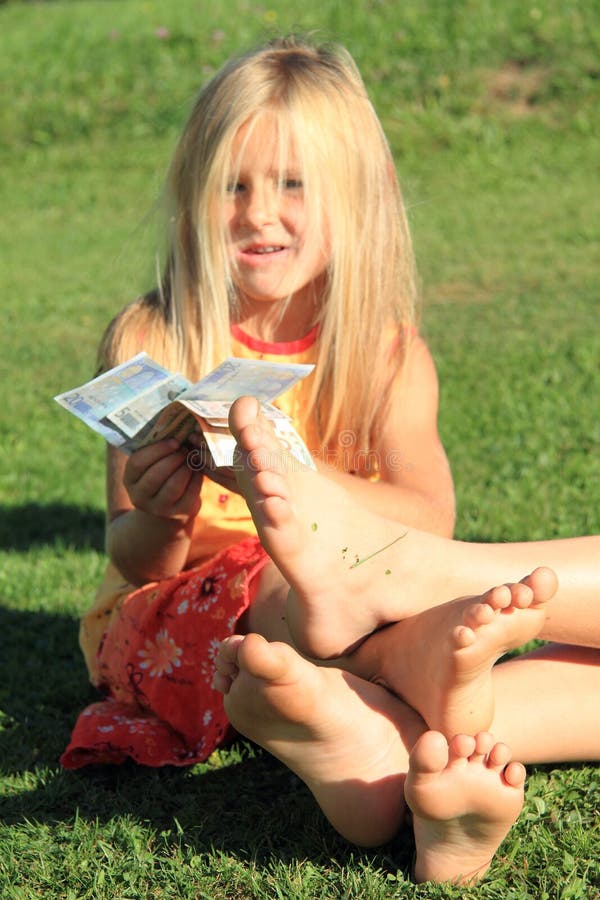Four soles of bare feet of little girl and boy playing on grass with euro money. Four soles of bare feet of little girl and boy playing on grass with euro money