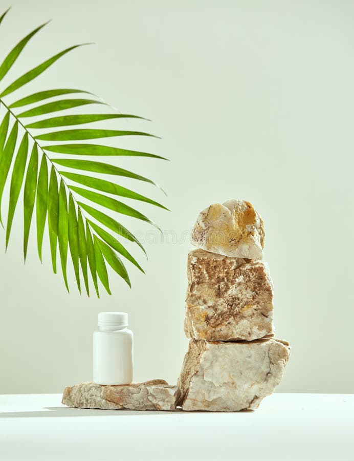 Podium of marble stones with mockup plastic jar, green palm leaf. Presentation of natural dietary supplement, vitamins for skincare. High quality photo