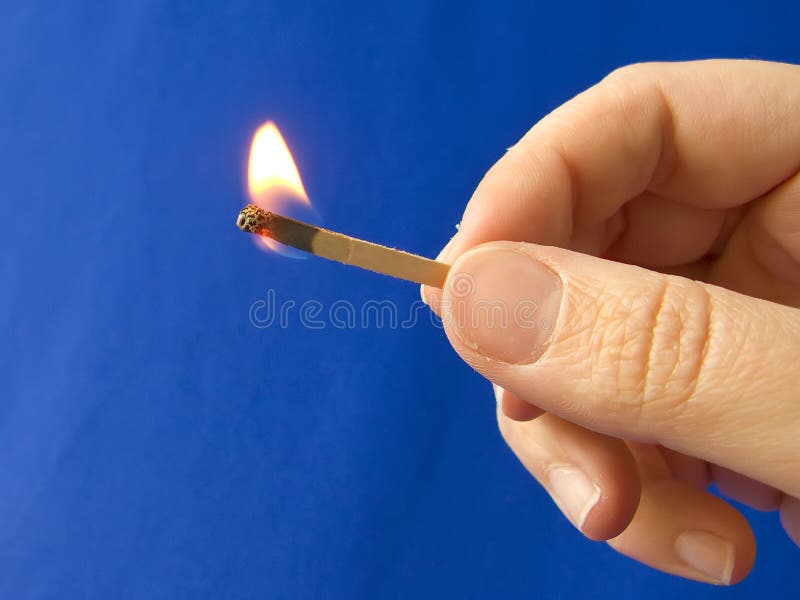 A hand holding a fired matchstick over blue background. A hand holding a fired matchstick over blue background