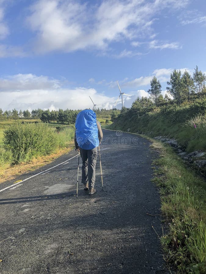 Podróżnik z plecakiem i trekking wtyka iść zmieloną drogę, słoneczny dzień, wzgórza z silnych wiatrów generatorami, niebieskie ni zdjęcie stock Podróżnik z plecakiem i trekking wtyka iść zmieloną drogę, słoneczny dzień, wzgórza z silnych wiatrów generatorami, niebieskie ni zdjęcie stock